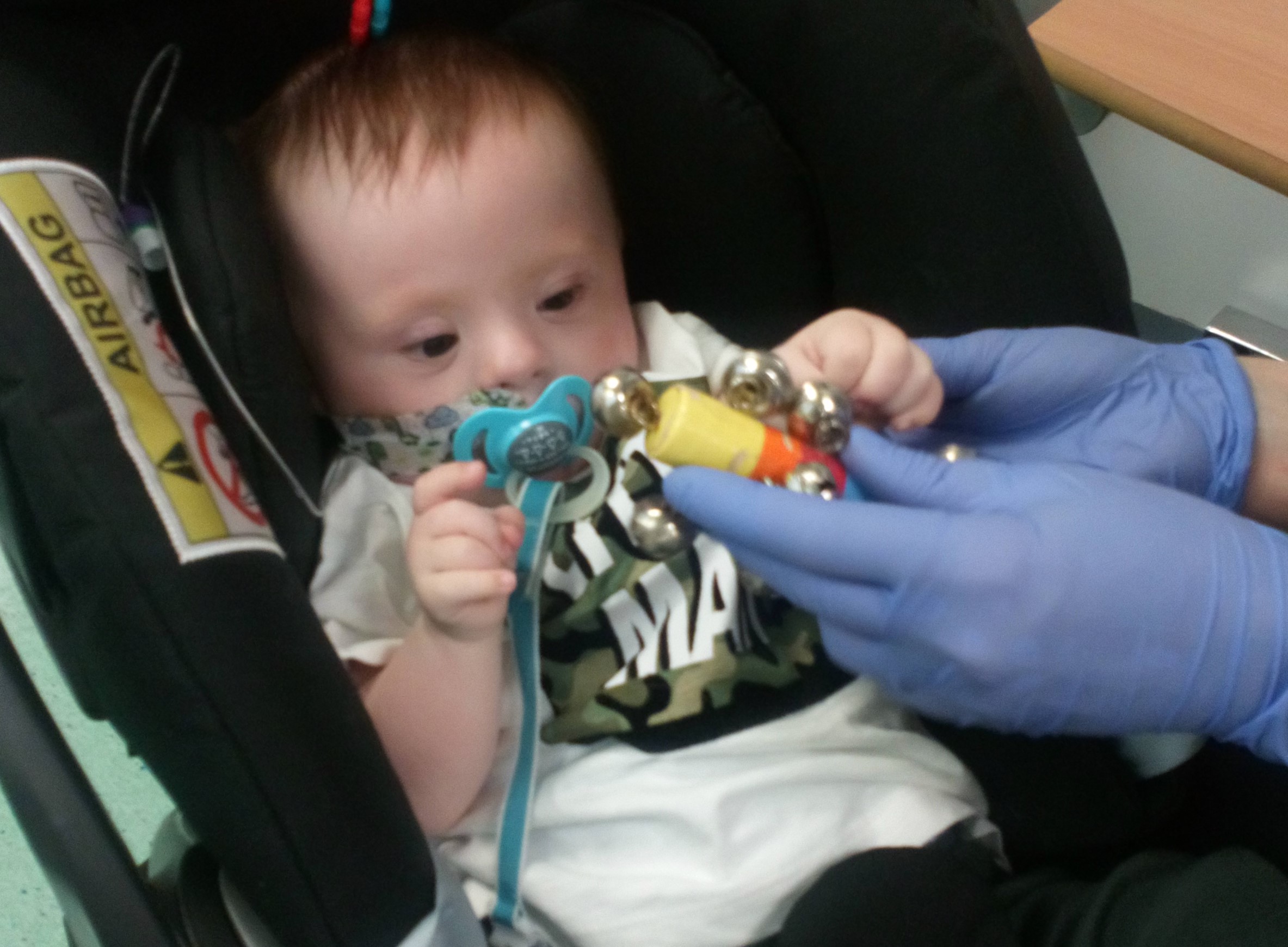 Baby sitting in a car seat batting a toy held up by a nurse