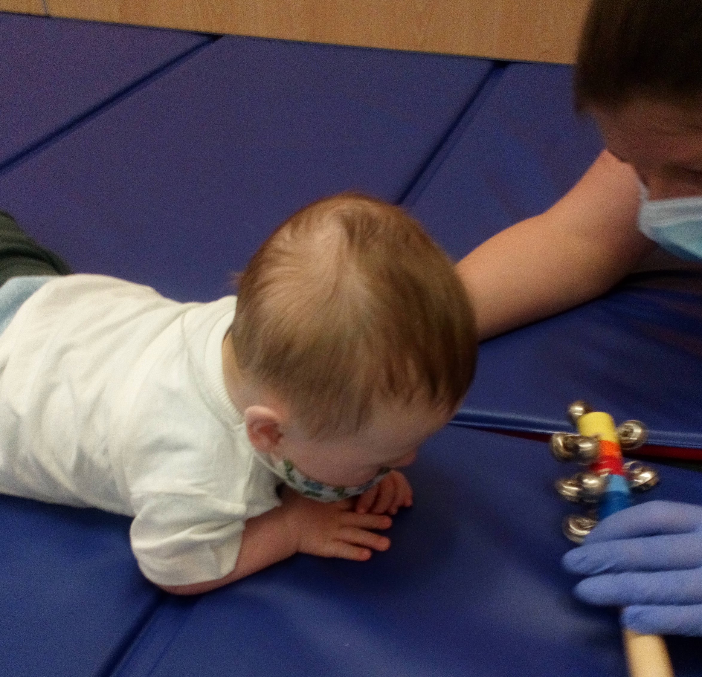 Baby on its tummy looking up at adult with toy