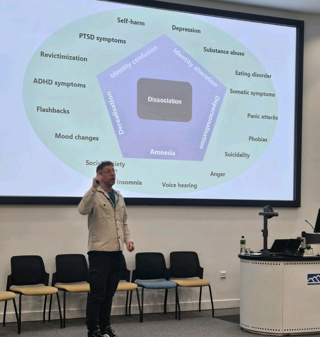 Psychologist Paul Langthorne presenting at a conference on dissociation, in front of a screen with a PowerPoint slide